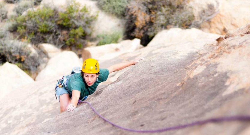 From above, a person wearing safety gear climbs towards the camera. 